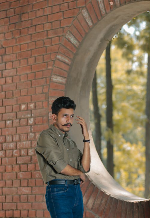 Young Man with Mustache Standing by a Brick Wall 