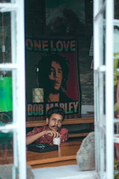 男人在舒适的咖啡馆里，一边喝咖啡，一边欣赏鲍勃·马利的海报