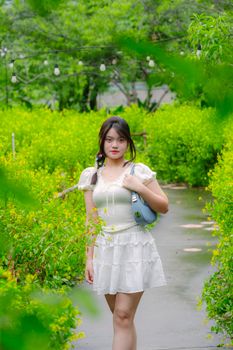 A young woman in a white dress walks through a vibrant green park on a summer day.
