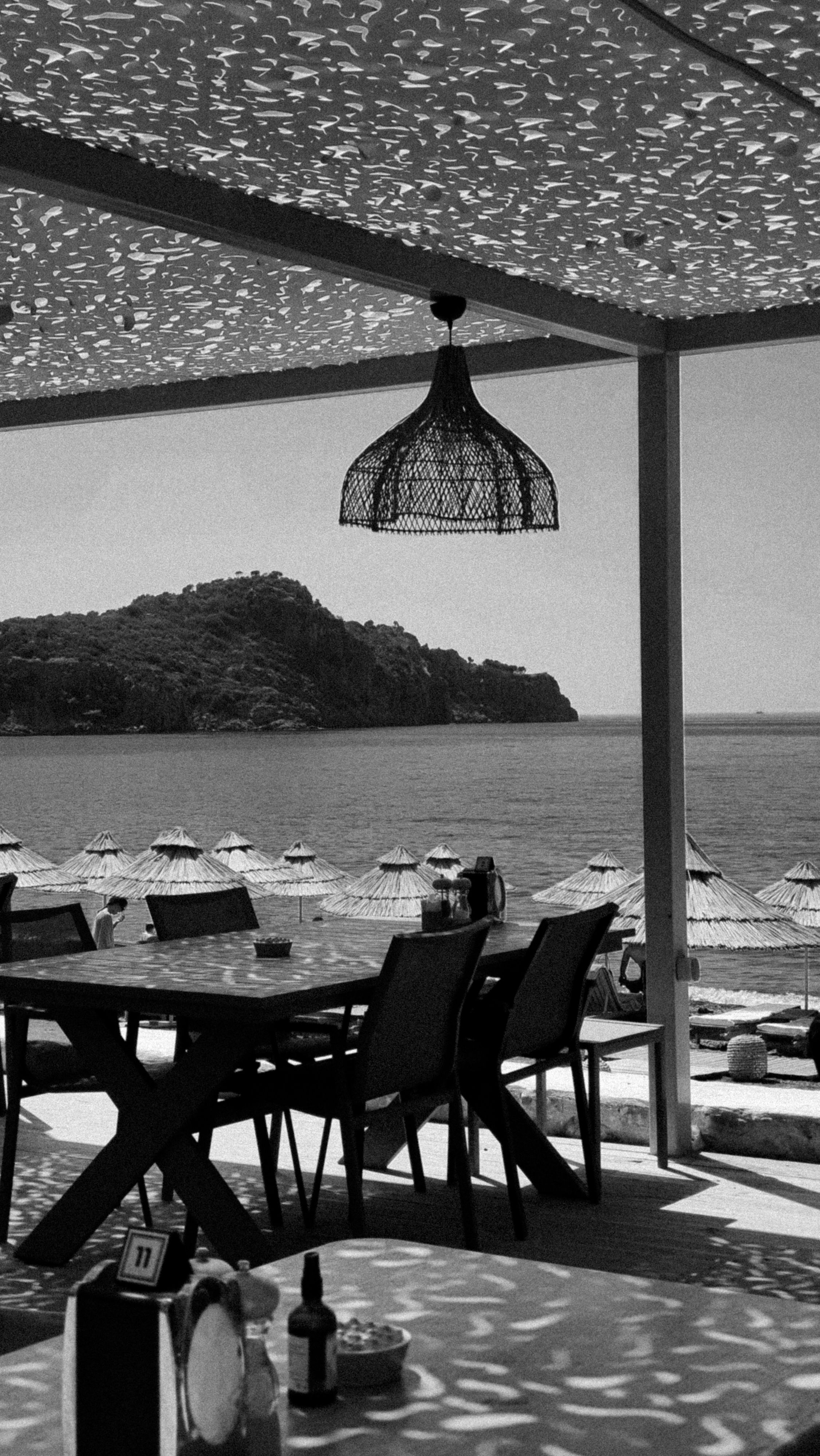 Black and white photo of a beachfront restaurant with umbrellas and sea view, creating a serene ambience.