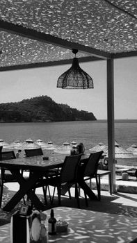 Black and white photo of a beachfront restaurant with umbrellas and sea view, creating a serene ambience.