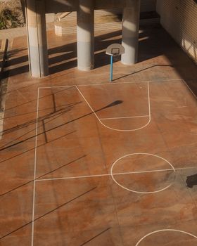 Empty urban basketball court with shadows and concrete columns in Bilbao, Spain.