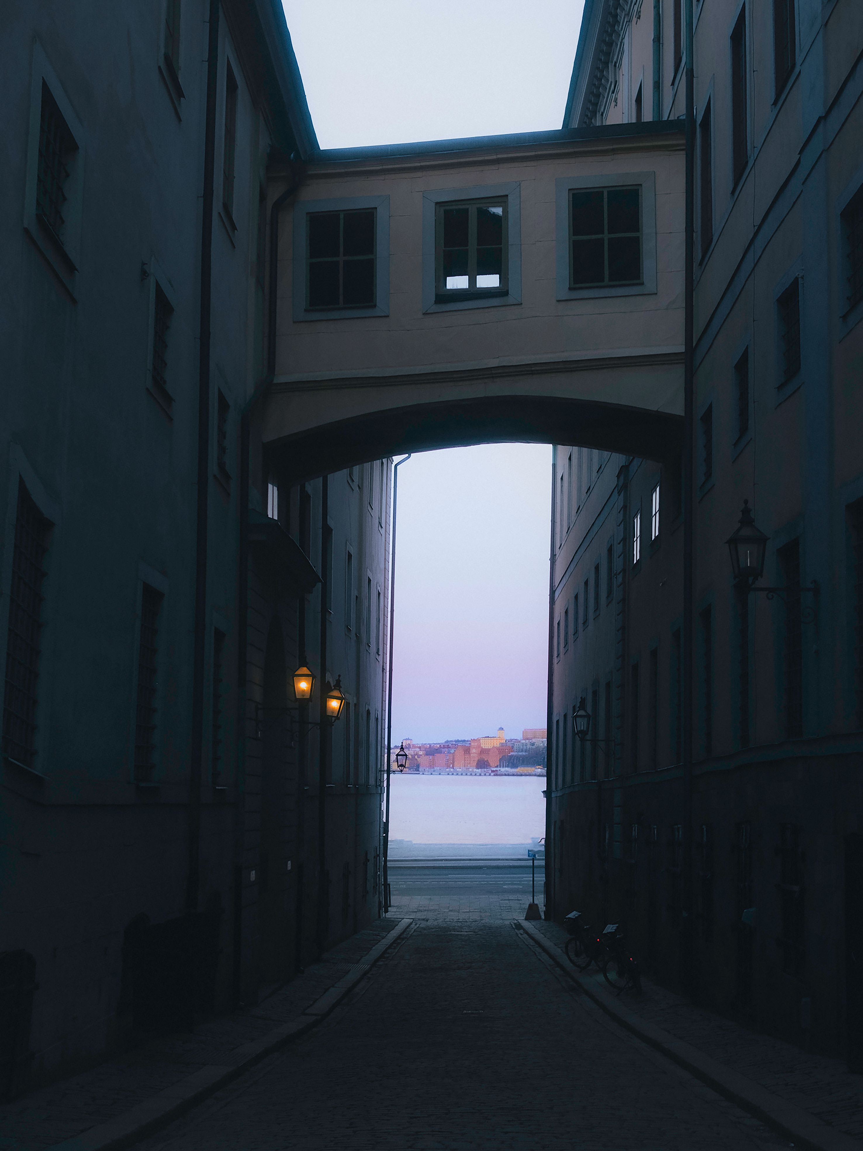 A scenic view from a narrow alleyway in Stockholm, revealing water and distant buildings at twilight.