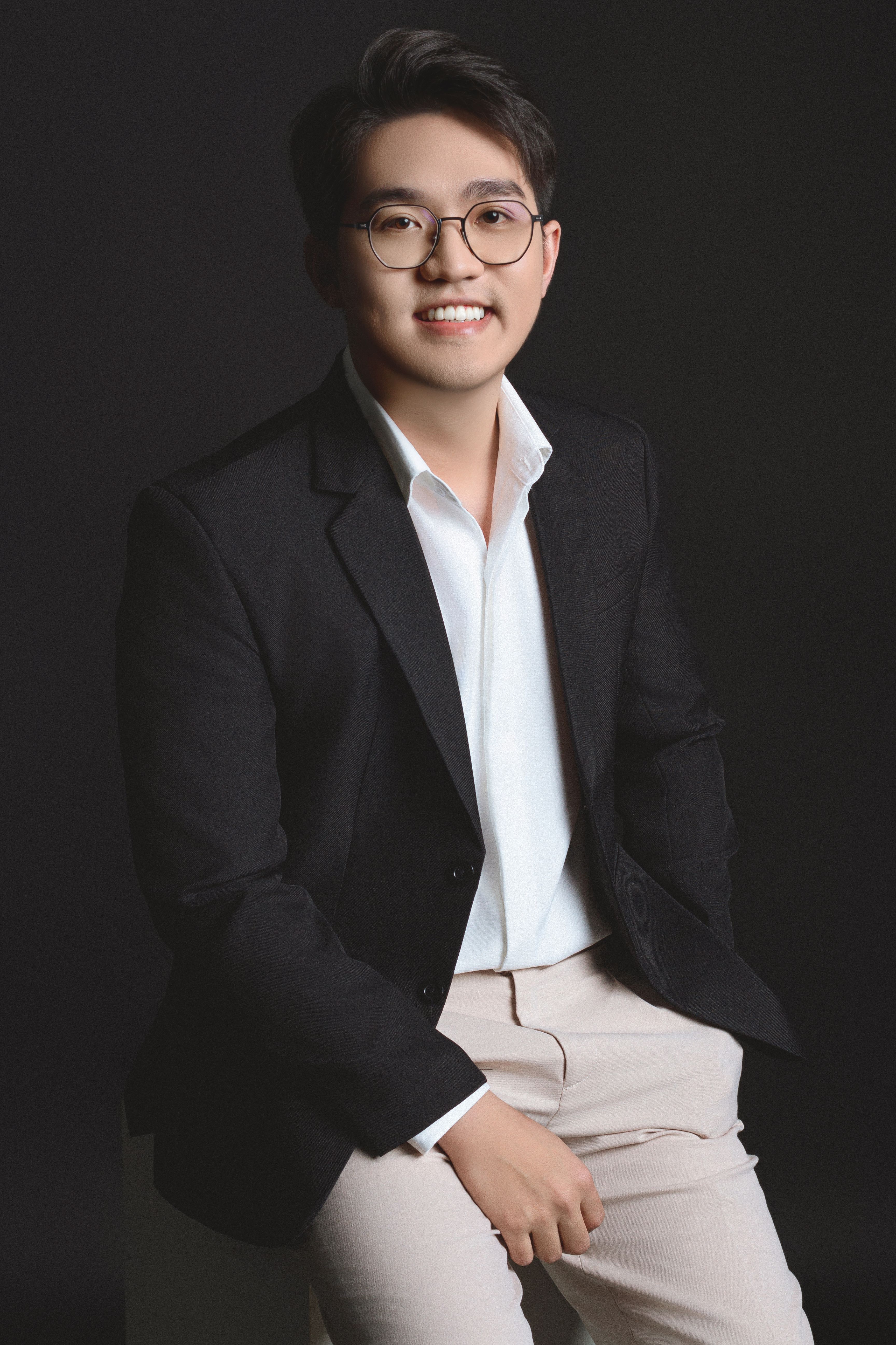 Elegant portrait of a smiling man wearing a black blazer and glasses in a studio setting.