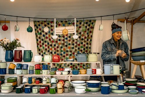 Free Vibrant display of handmade pottery with a smiling vendor at a market stall. Stock Photo
