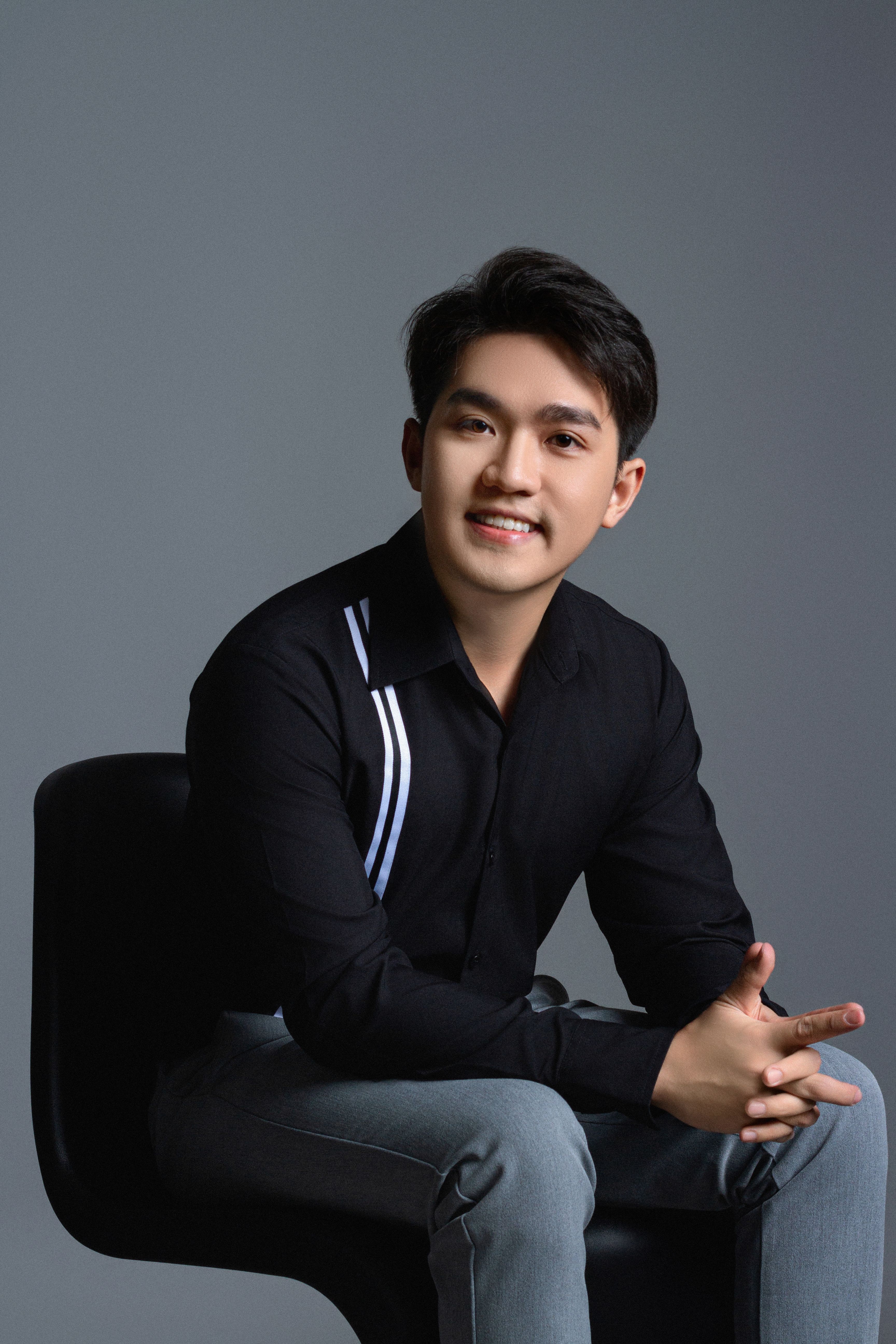 Portrait of a smiling young man in a black shirt sitting in a studio environment.