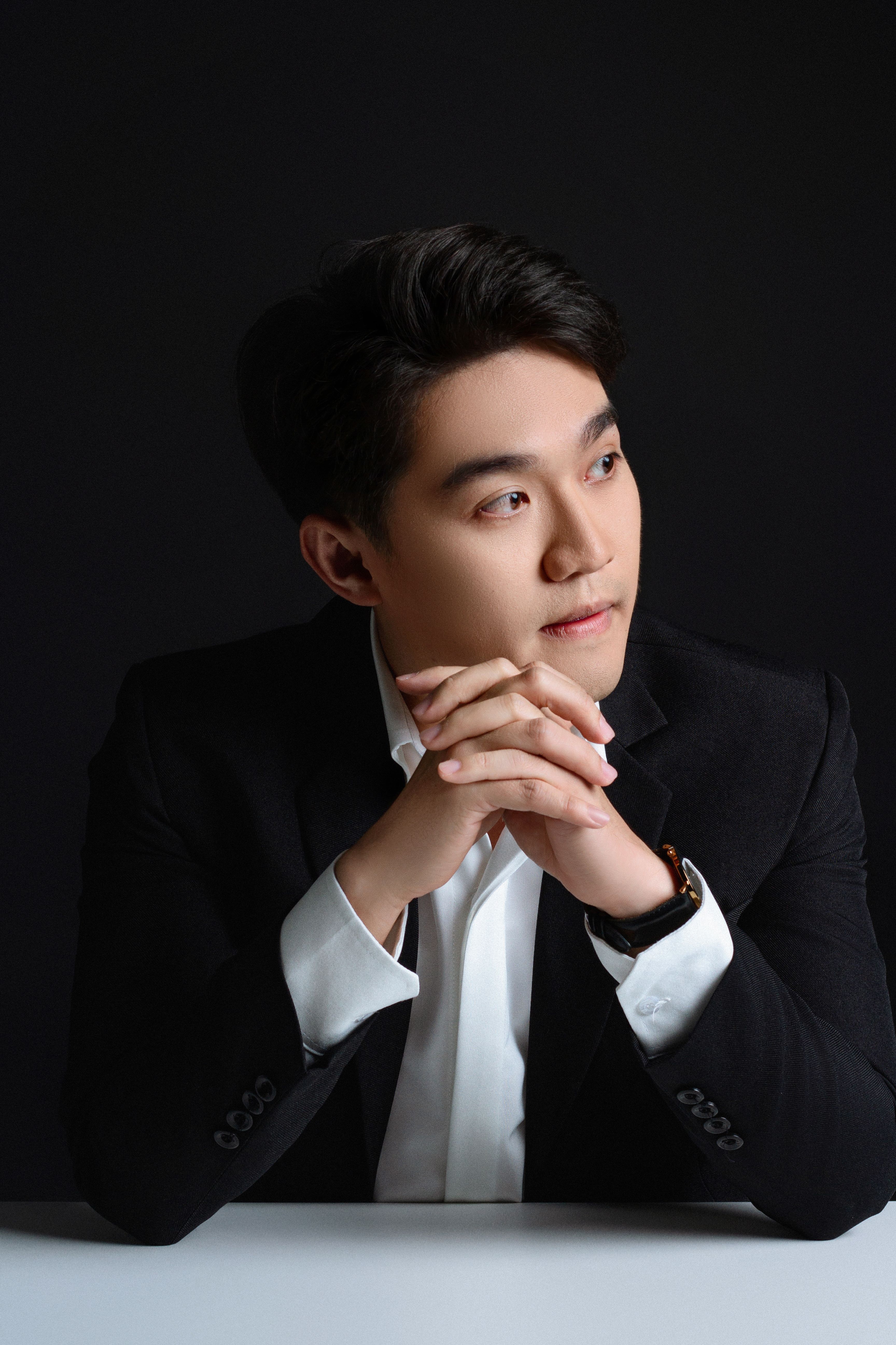 Studio portrait of a confident businessman in a black suit with hands clasped thoughtfully.
