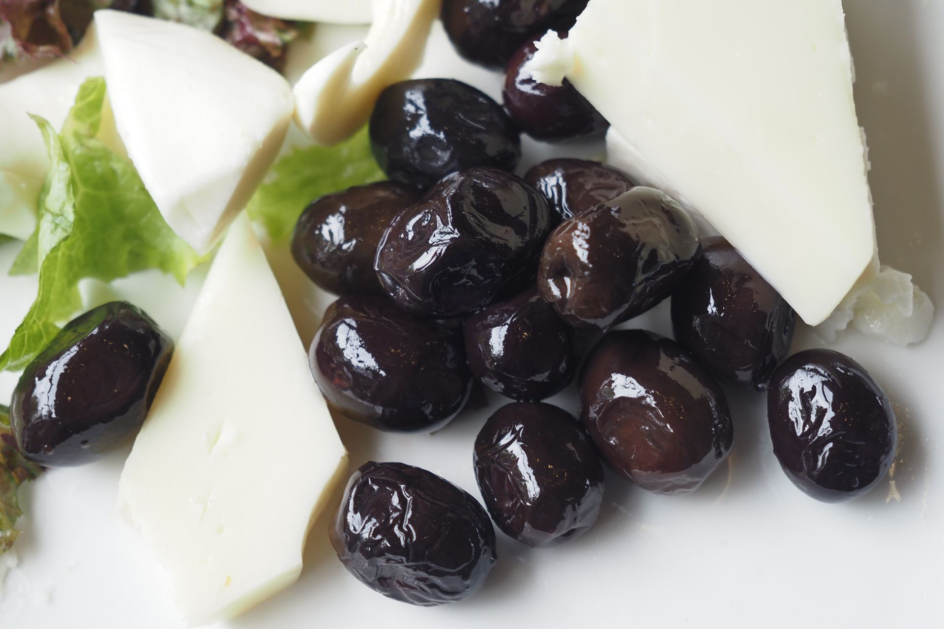 Close-up of fresh cheese slices with black olives and lettuce on a white plate, ideal for food photography.