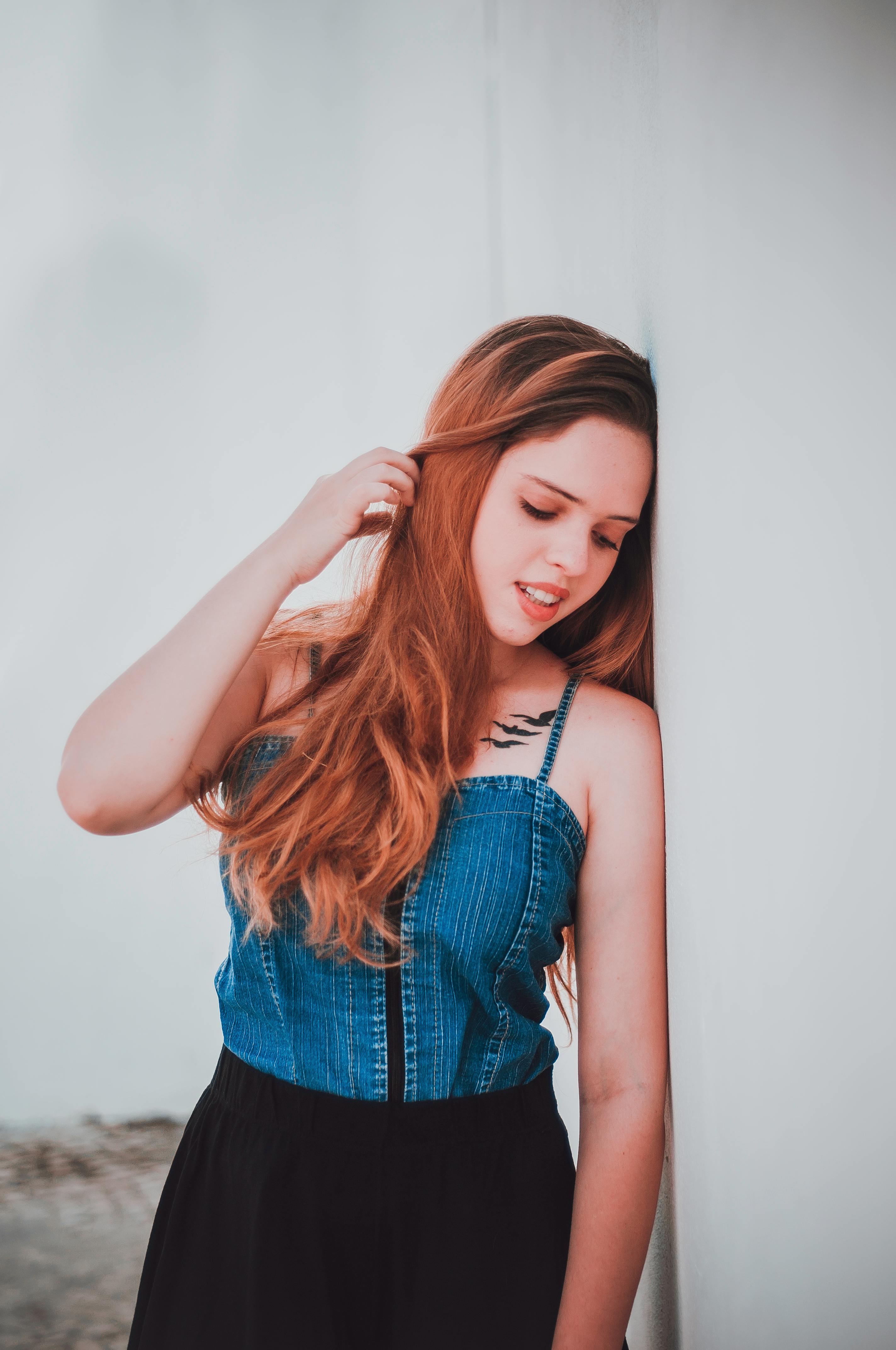 一名年轻女子身穿牛仔上衣，站在户外，抚摸着头发