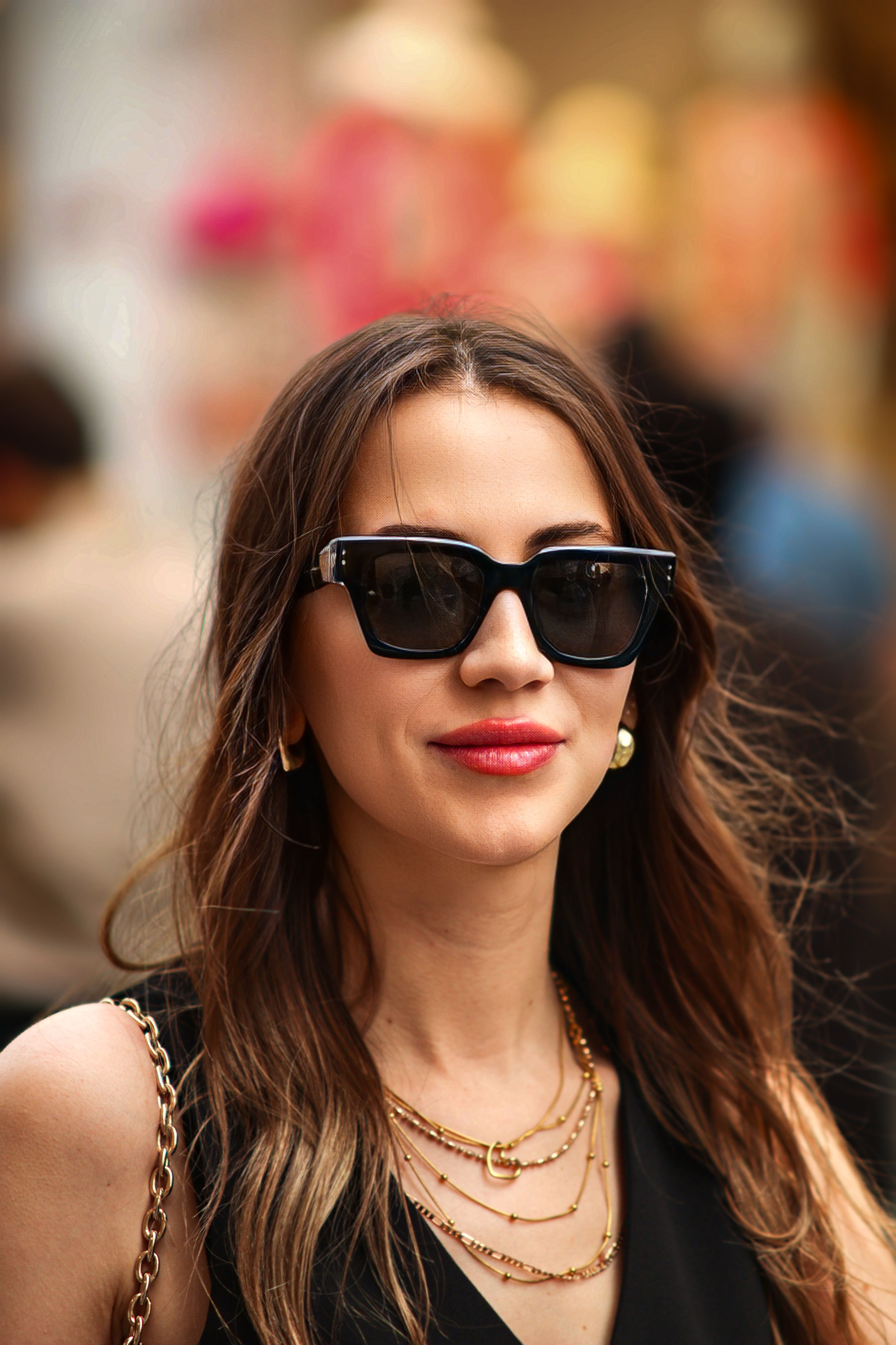 Portrait of a brunette woman wearing sunglasses and layered necklaces, exuding elegance and sophistication.