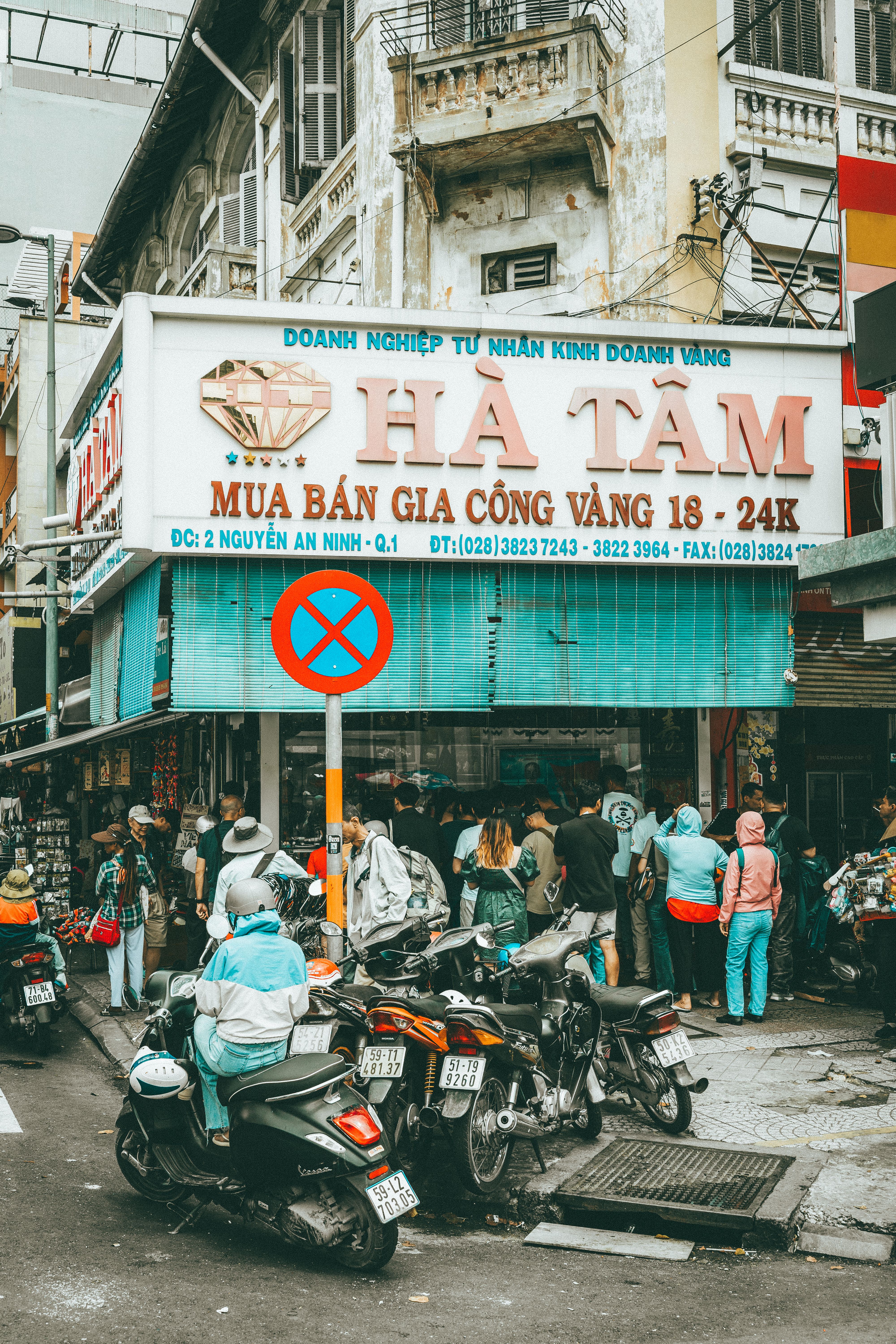 Crowded urban street corner in Ho Chi Minh City with motorbikes and pedestrians.
