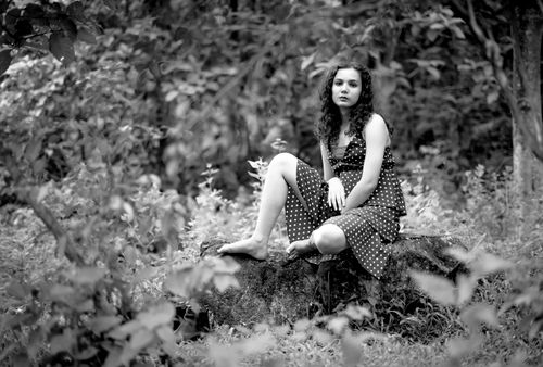 Free Stunning black and white portrait of a woman sitting barefoot on a rock in a lush forest. Stock Photo