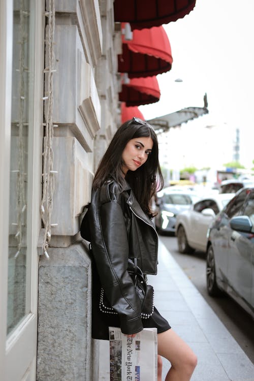 A woman in a black leather jacket leaning against a wall
