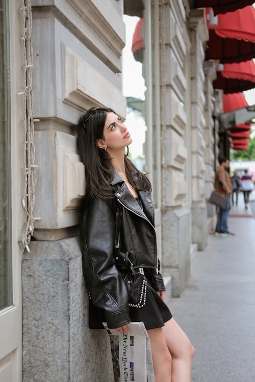 A woman in a black leather jacket leaning against a wall