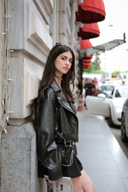 A woman in a black leather jacket leaning against a wall
