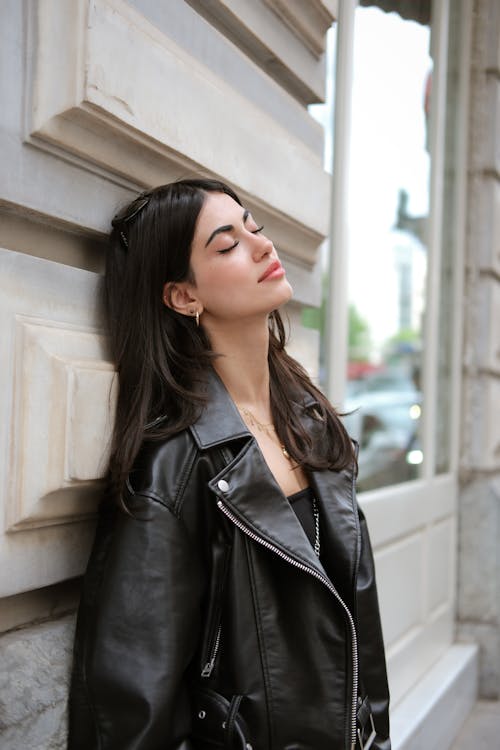 A woman in black leather jacket leaning against a wall