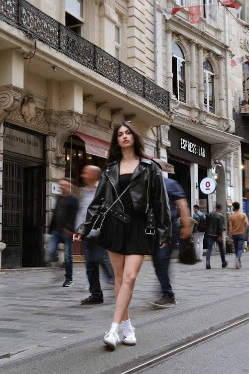 A woman in a black leather jacket and white sneakers walking down a street