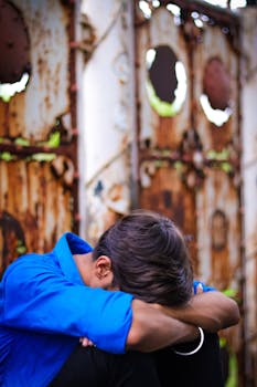 一个穿着蓝色衬衫的年轻人，将头靠在生锈的金属门上，显得若有所思