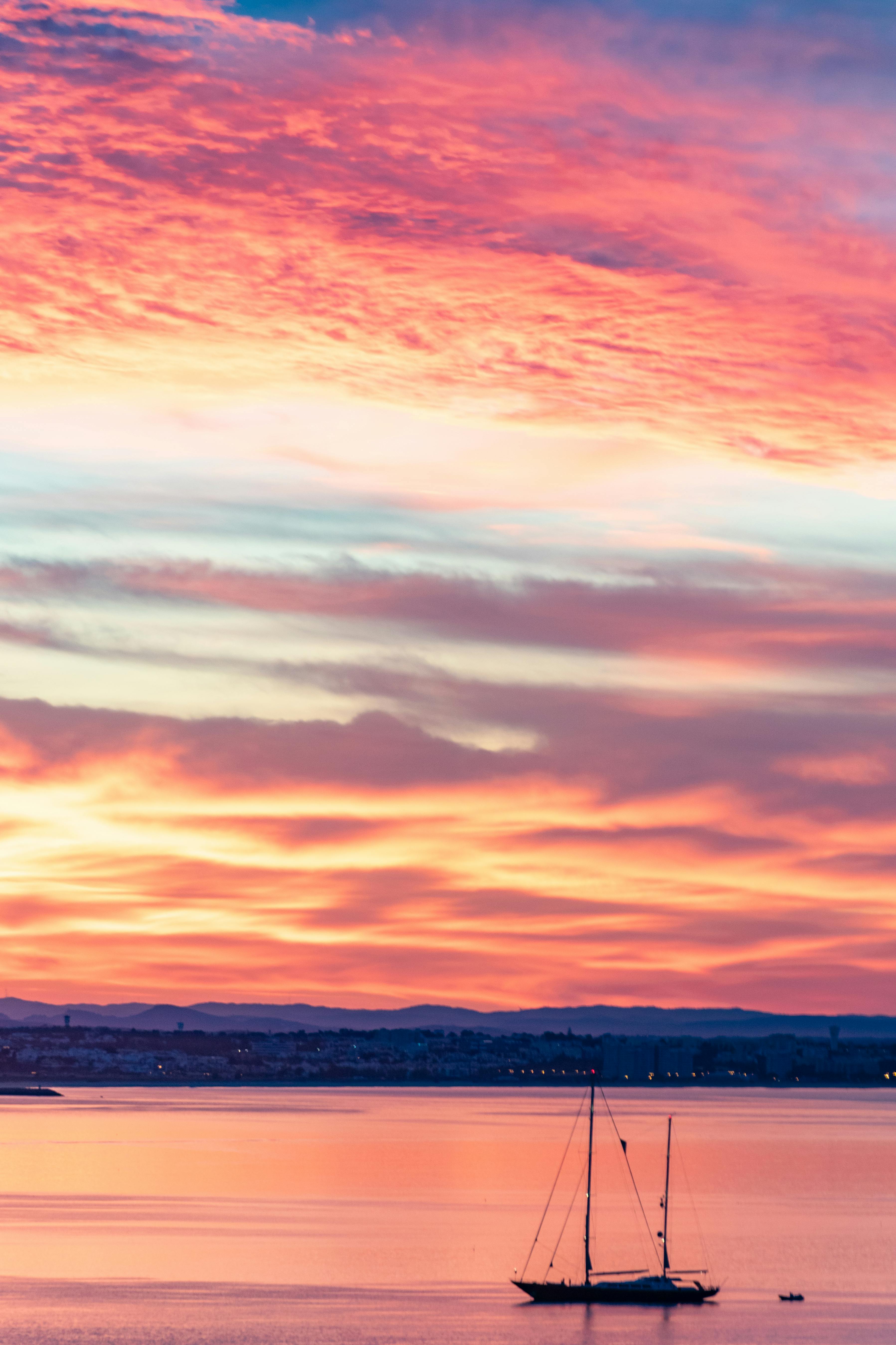 在葡萄牙拉各斯附近，一艘宁静的帆船剪影映衬着充满活力的日落天空
