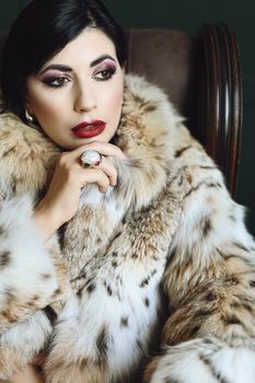 A stylish woman in an exquisite fur coat poses thoughtfully, showcasing high fashion and elegance.