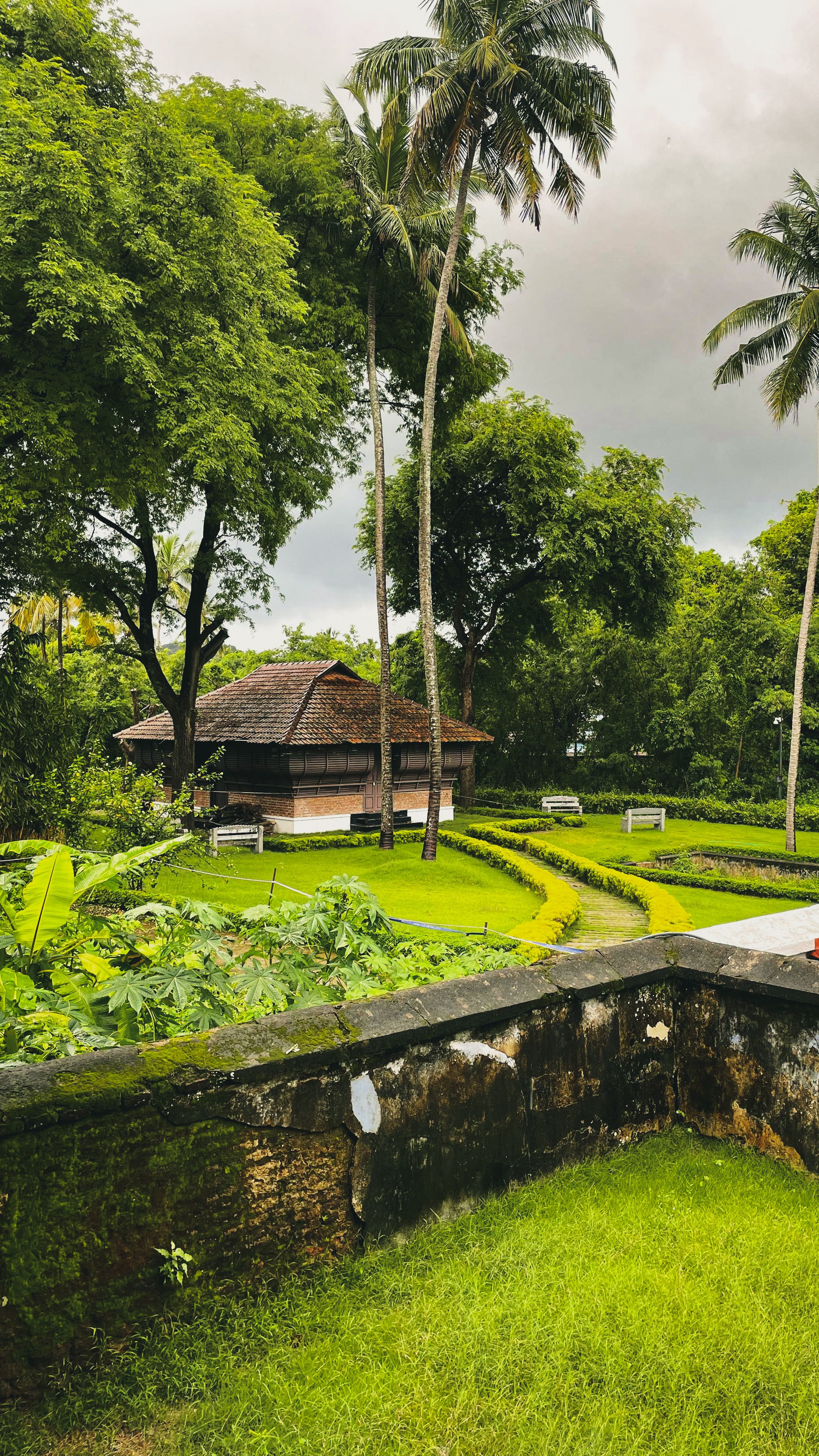 Serene park setting in Kanniyakumari with traditional building and tropical plants.