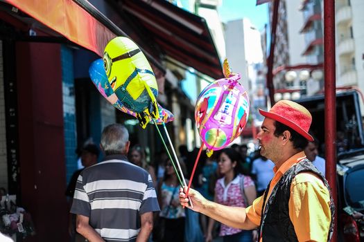 Colorful street performer holding balloons in a vibrant São Paulo market scene.