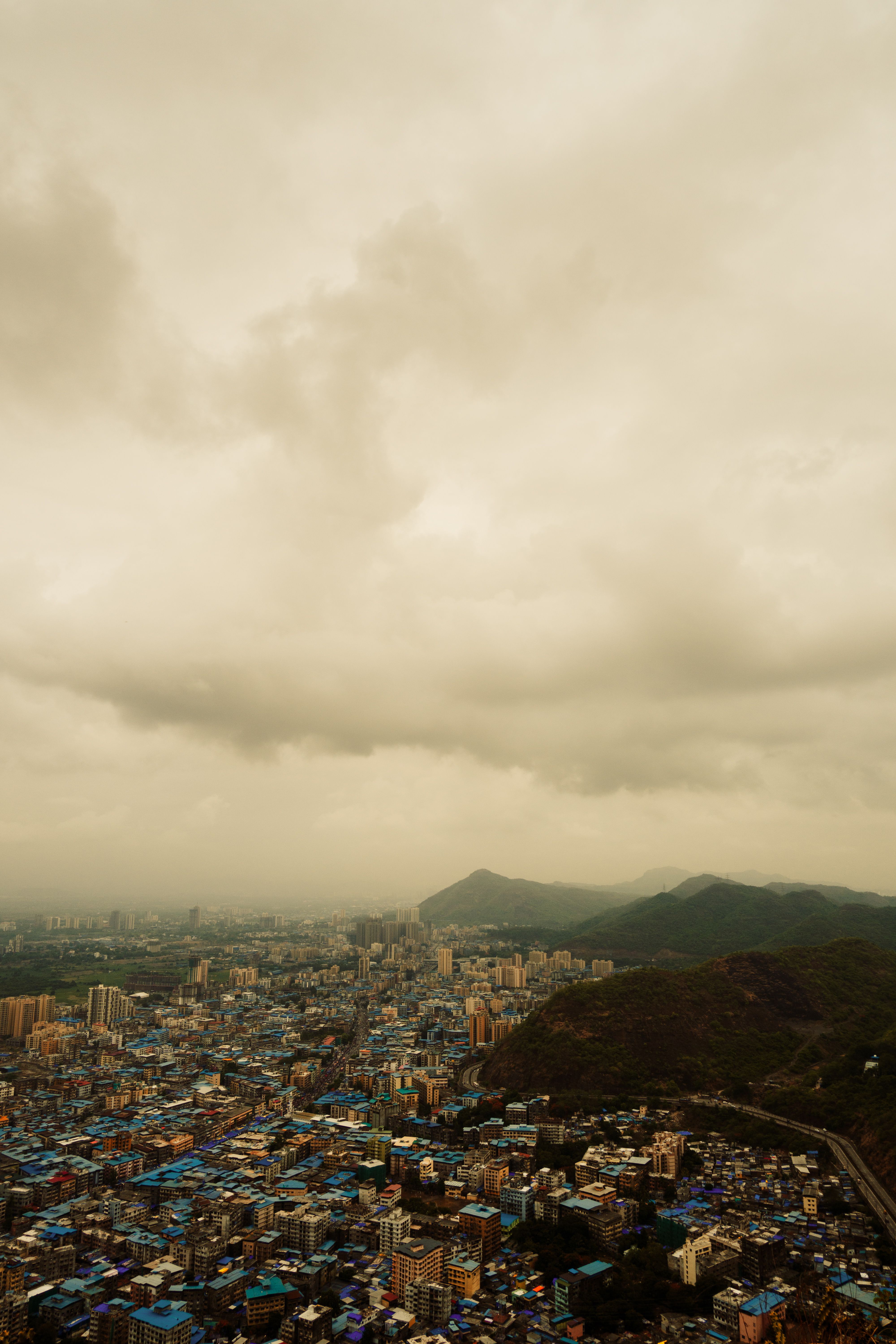 Dramatic aerial shot of a sprawling cityscape with mountains and cloudy sky.