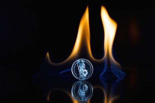 Round Silver-colored Coin on Black Surface With Flame