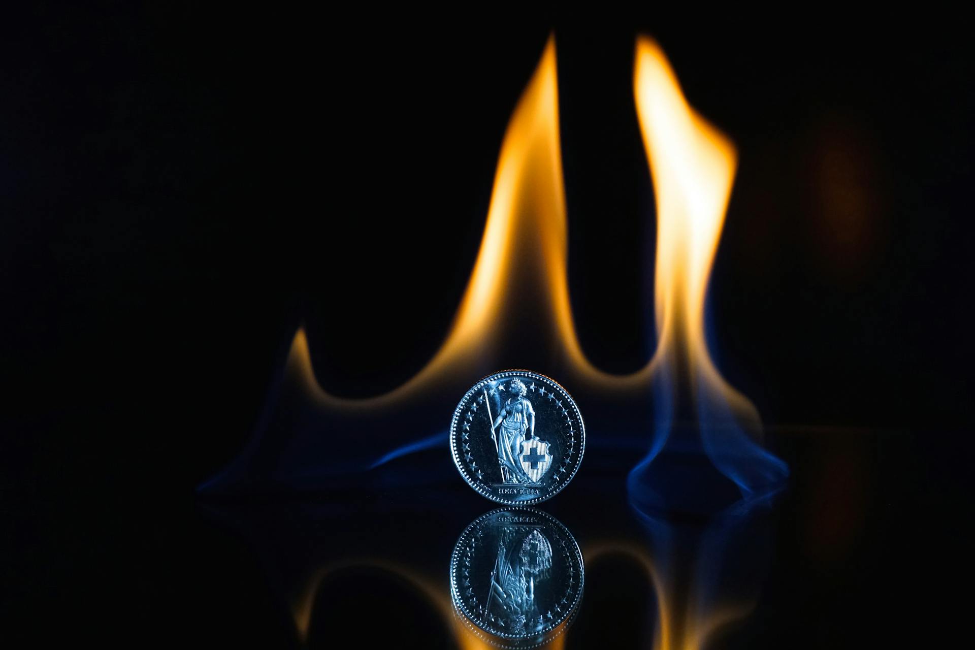 Round Silver-colored Coin on Black Surface With Flame