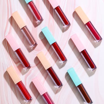 Stylish flatlay of red and nude liquid lipsticks on a marble surface, perfect for beauty themes.