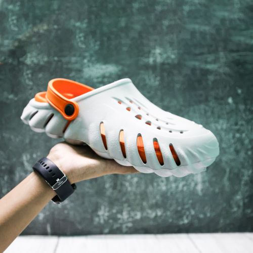 Free Close-up of a hand holding a stylish white and orange clog shoe against a textured background. Stock Photo