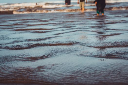 Close-up of gentle beach waves with people in the background at sunset, capturing a serene coastal moment.