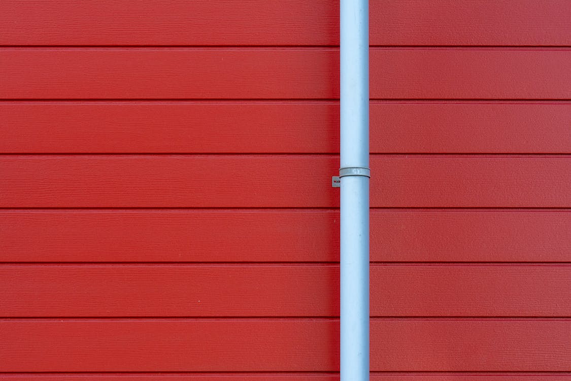A metal pipe on a red wall with a red door