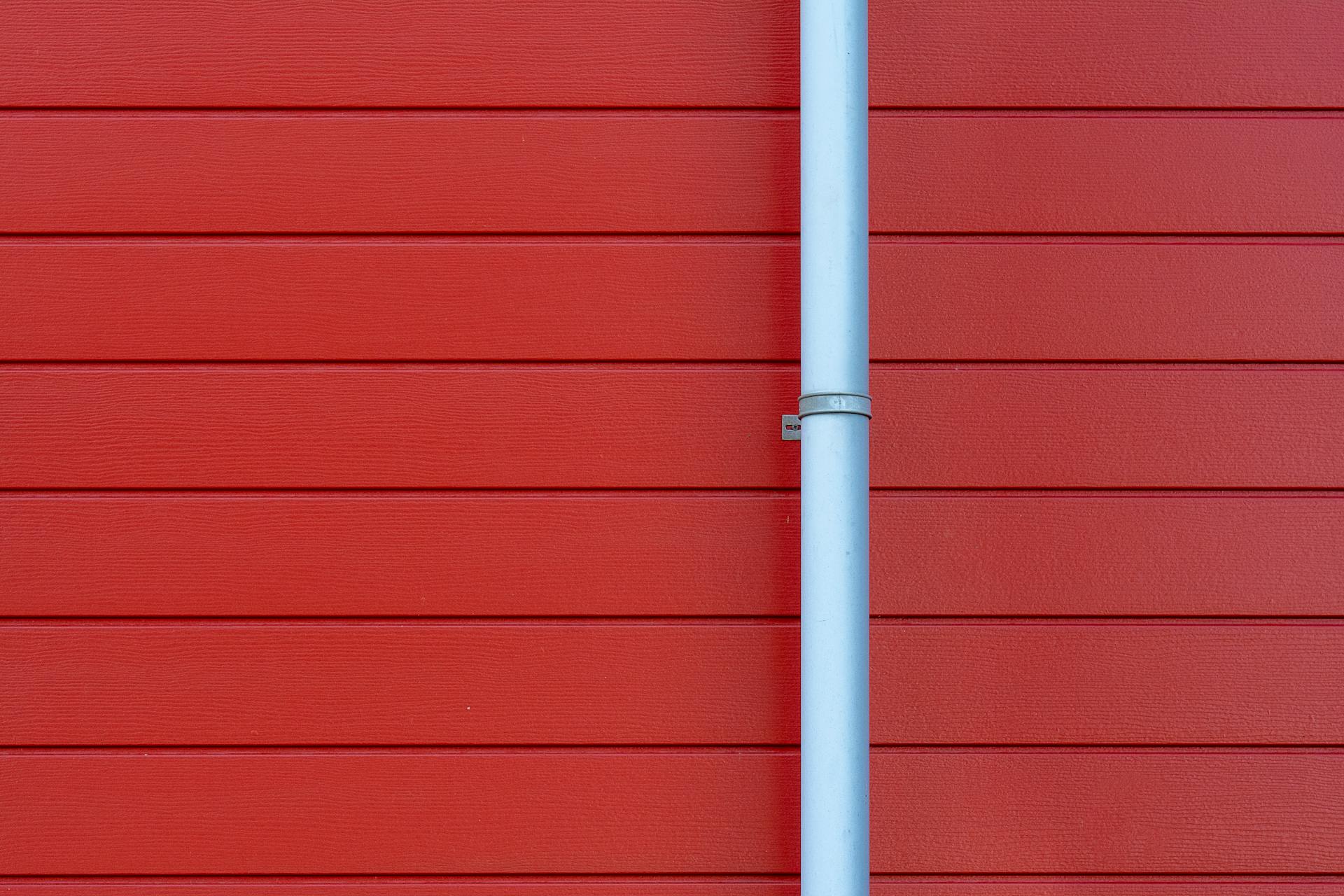 A minimalist photo of a red wall with a white rain gutter, showing clean lines and vibrant color contrast.