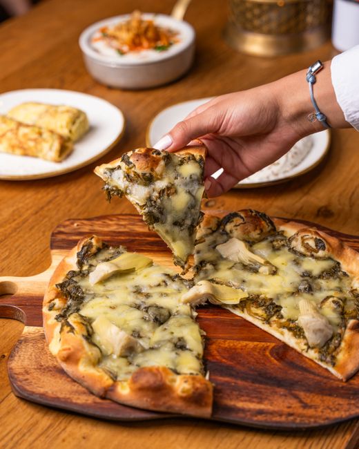 A bubbling spinach artichoke dip in a round baking dish with a golden, lightly browned Parmesan crust and a tortilla chip dipped into the edge.