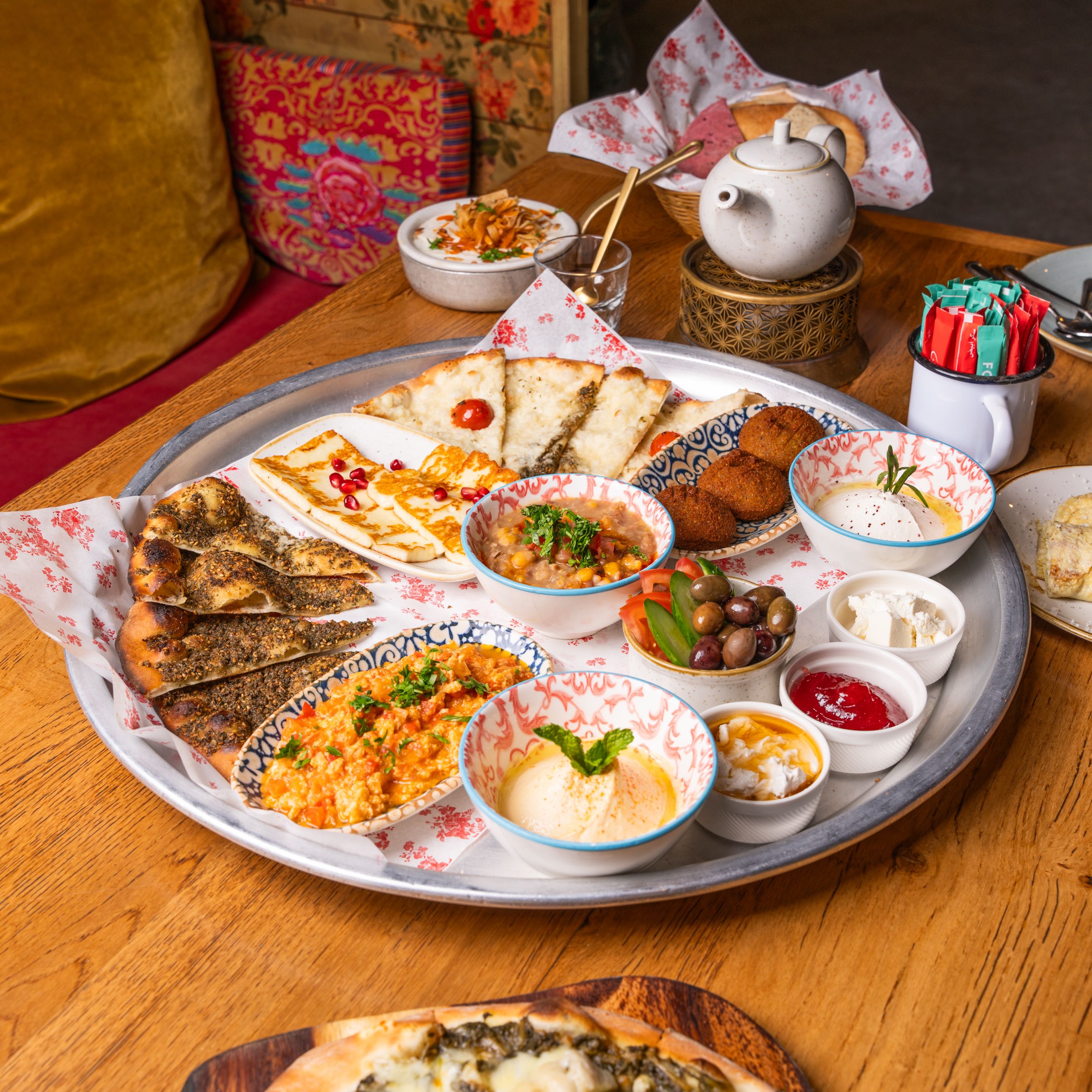 Platter of Middle Eastern breakfast dishes with teapot on a wooden table.