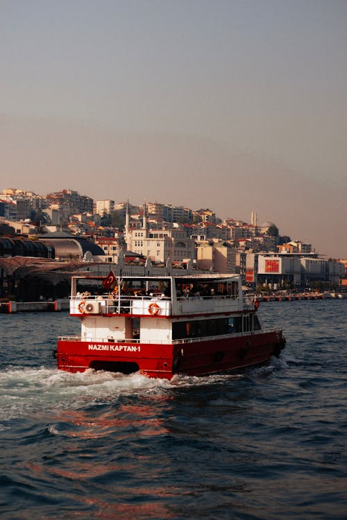 A red boat traveling down a river near a city