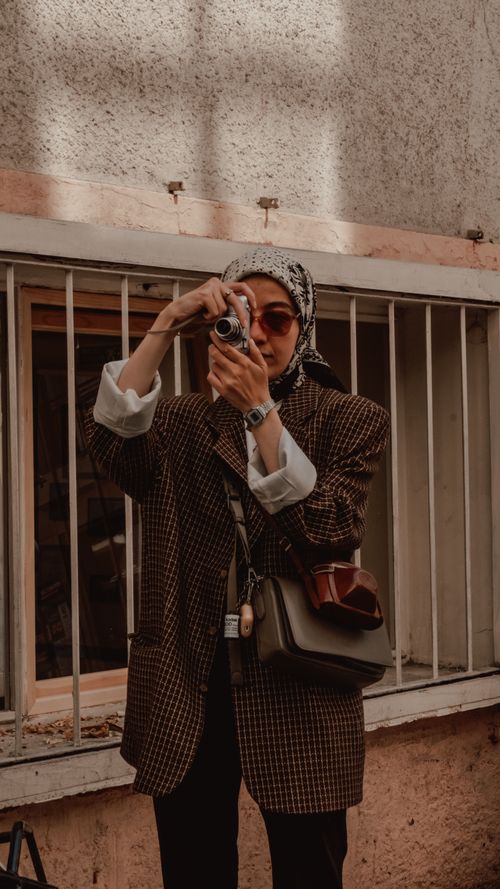 Free Stylish woman wearing hijab and sunglasses captures a photo outdoors with vintage camera. Stock Photo