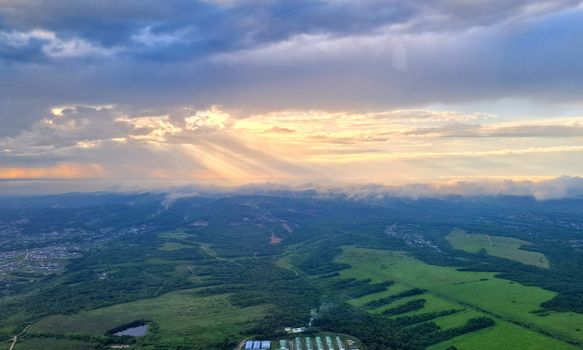 Stunning aerial view of a rural landscape with sun rays piercing through clouds at sunset.