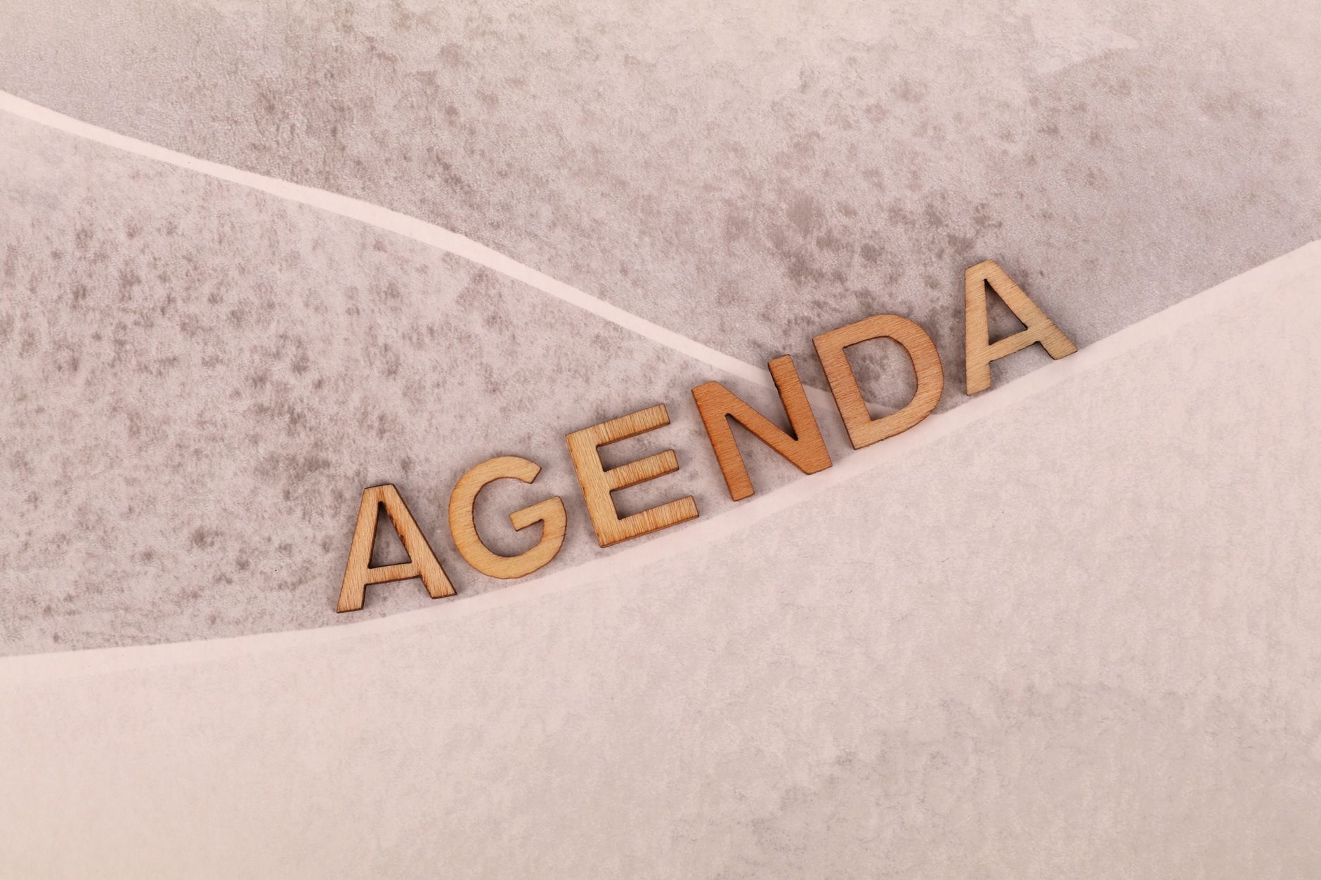Wooden letters spelling 'agenda' on a textured beige background with an abstract design.