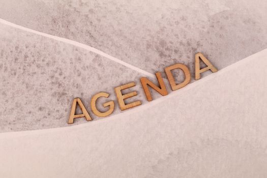 Wooden letters spelling 'agenda' on a textured beige background with an abstract design.