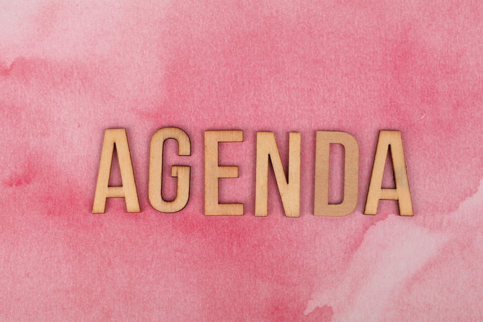 Wooden letters spelling 'Agenda' on a vibrant pink watercolor background.