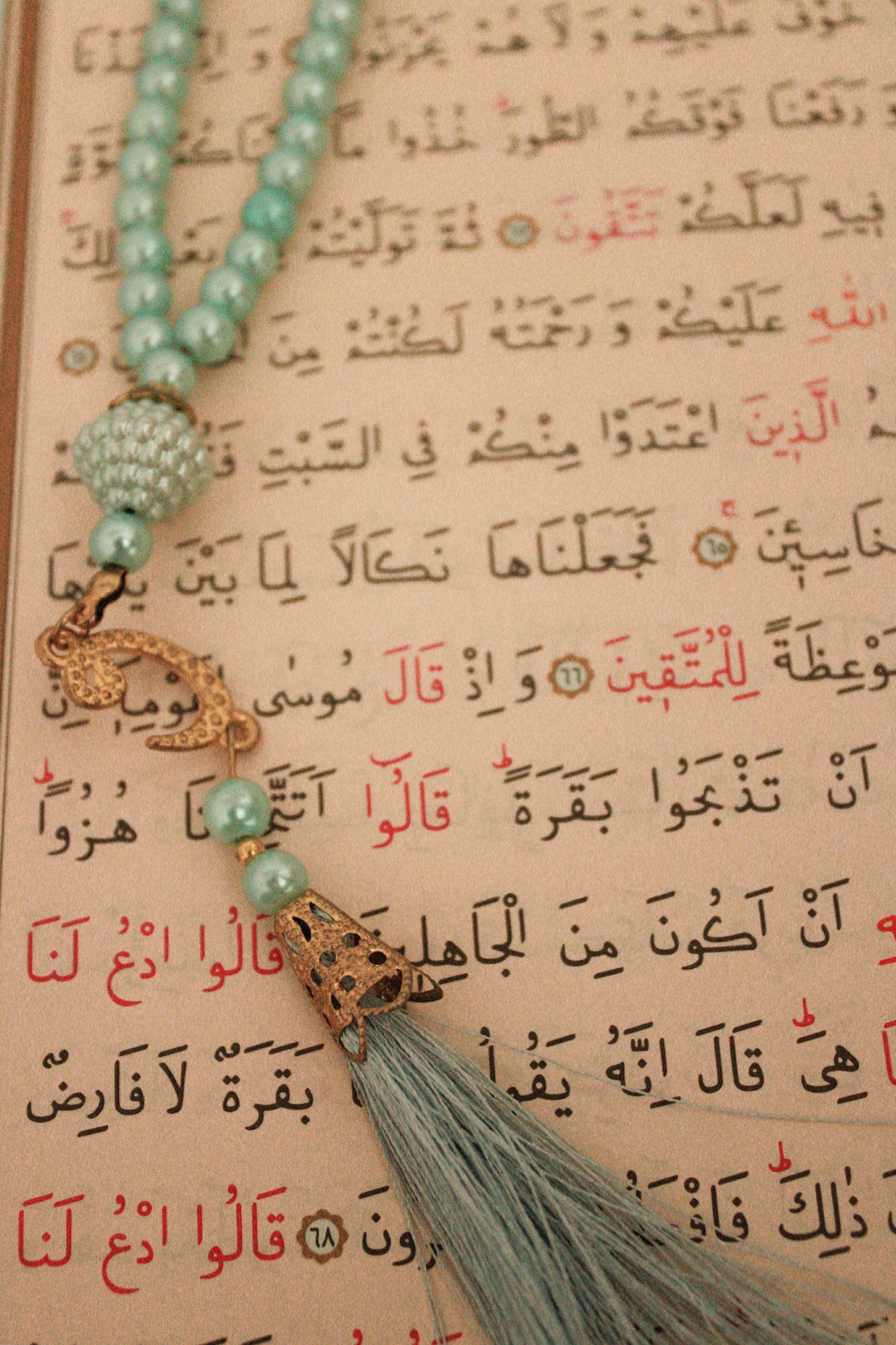 Detailed close-up of a Quran page with turquoise prayer beads signifying Islamic faith.