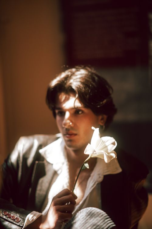 Free Young man in stylish attire holding a white flower, captured in soft light. Stock Photo