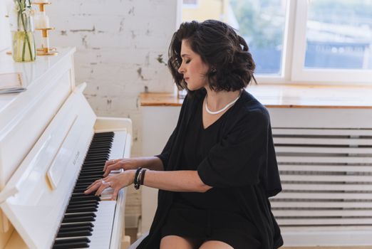 Brunette woman sitting and playing a piano in a well-lit room, showcasing musical elegance.