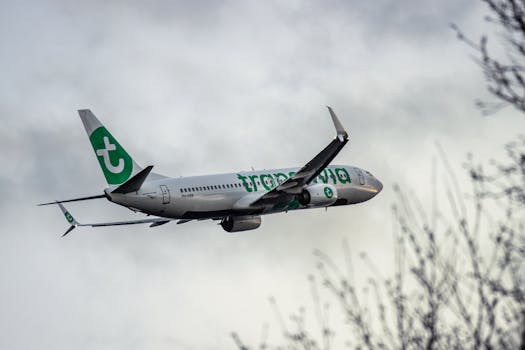 Low-angle shot of a Transavia aircraft flying through cloudy skies near Schiphol Airport.
