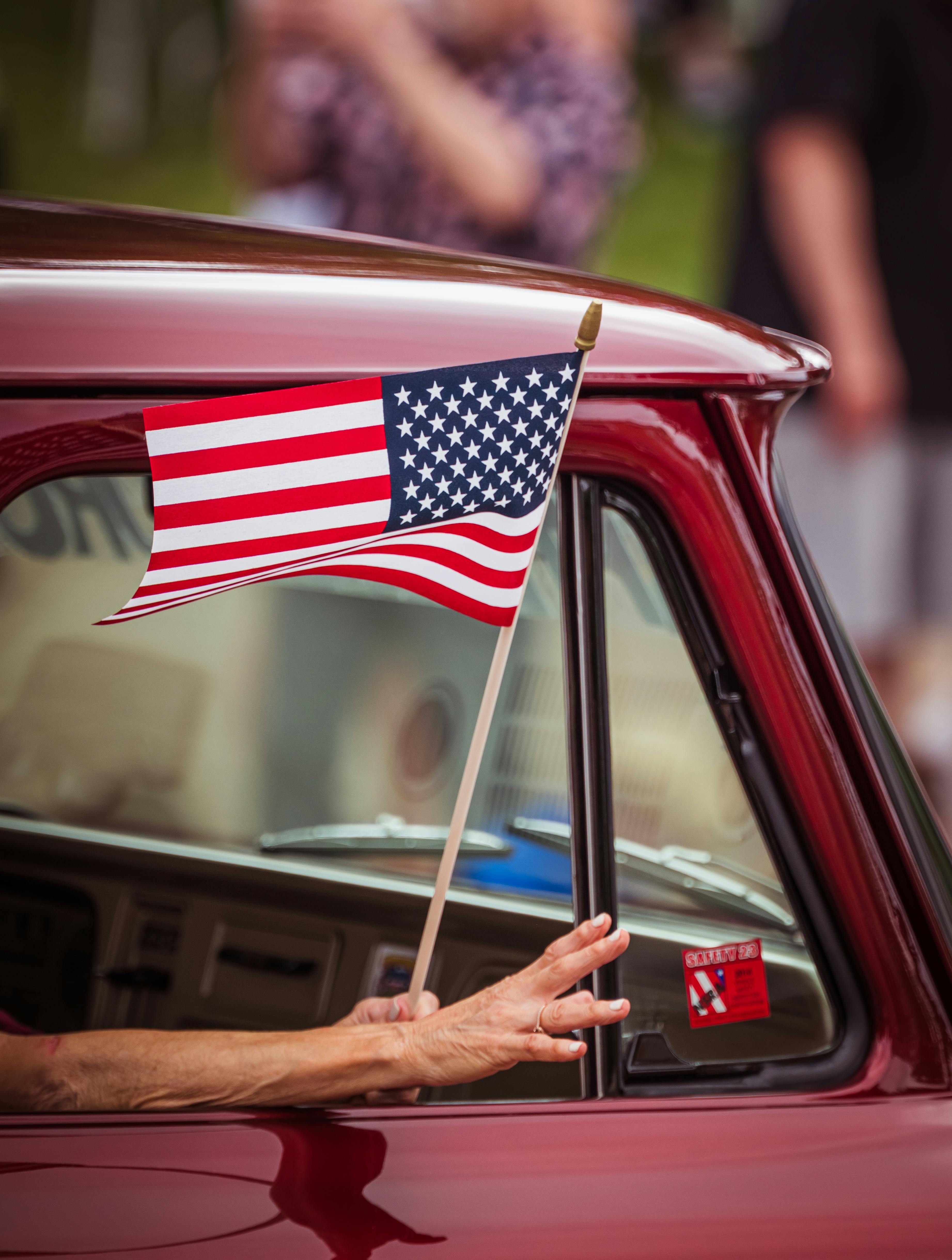 Hand waves an American flag from a vintage car window, capturing patriotic spirit.