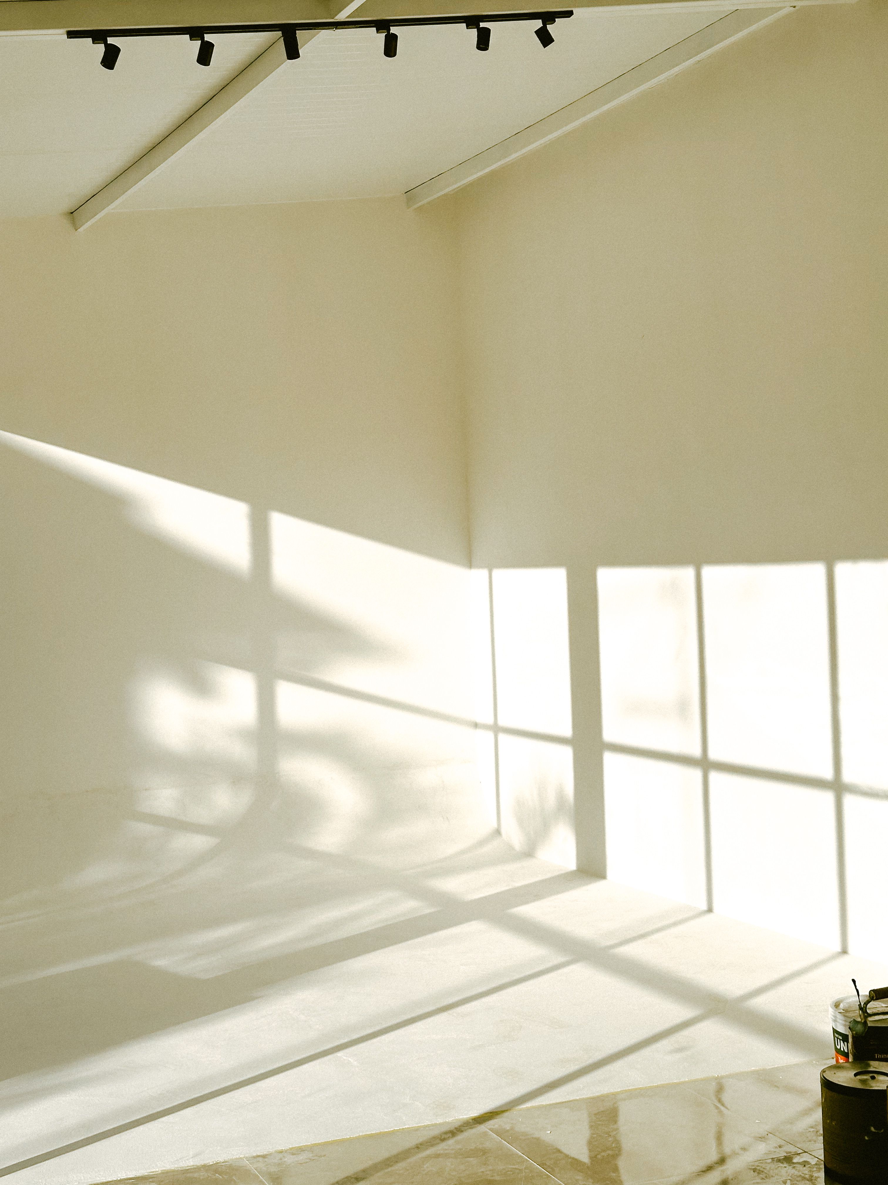 Bright, empty room with sunlight casting geometric shadows on white walls.