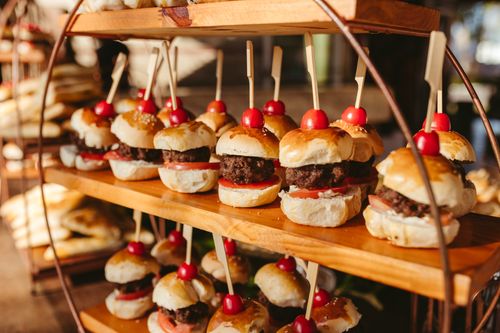 Free Close-up of freshly made mini burgers with tomatoes at an outdoor event setup. Stock Photo