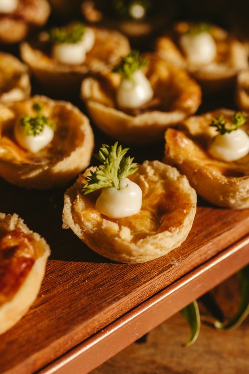 Free Delicious savory tartlets garnished with fresh herbs, presented on a wooden tray under warm lighting. Stock Photo